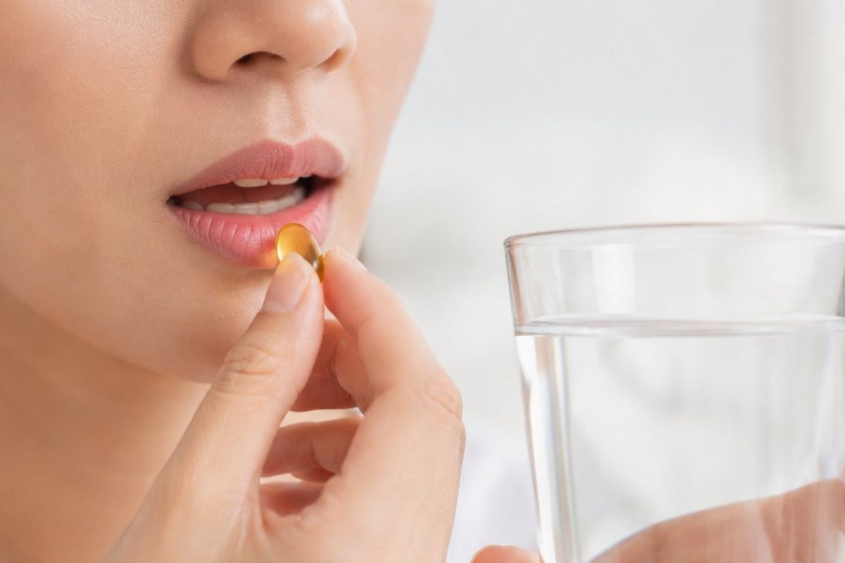 devojka stavlja u usta kapsulu ecomer forte i drži čašu sa vodom